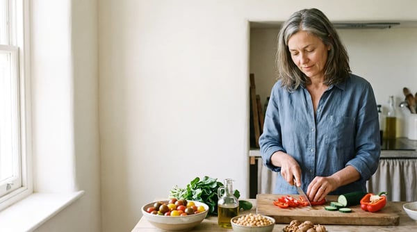 Frau um die 50 schneidet in einer hellen Küche Paprika und bereitet ein mediterranes Gericht mit Tomaten, Kichererbsen und Olivenöl zu